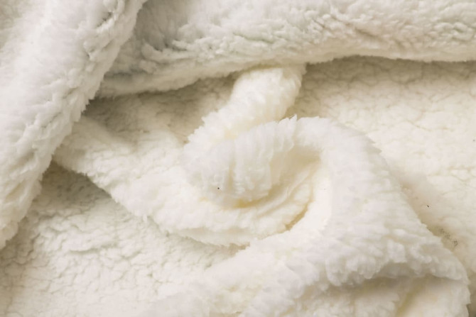 A soft, creamy white, unisex wearable blanket made from 100% polyester, featuring a textured, plush surface.