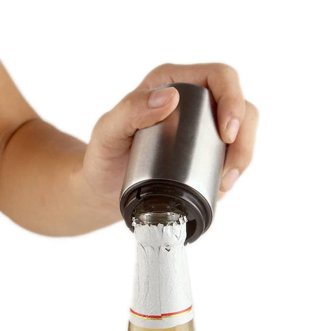 A drink bottle opener in stainless steel, being used to open a bottle with a white label.