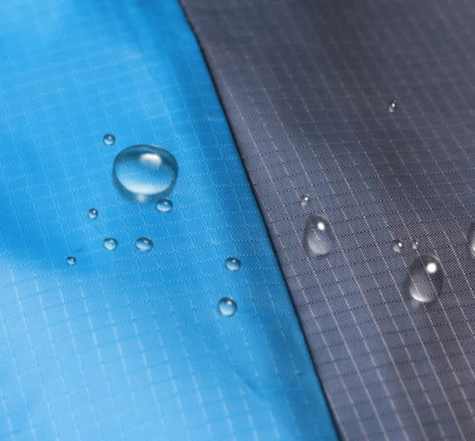 A water-resistant picnic blanket featuring a blue section and a grey section, with droplets of water on the surface.