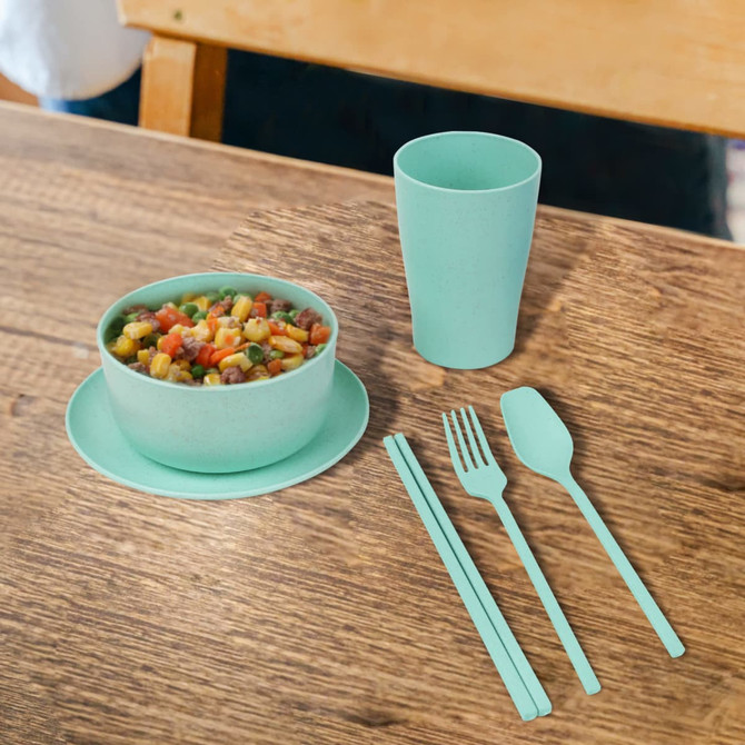 A mint green wheat straw tableware set featuring a bowl, plate, cup, fork, knife, and spoon on a wooden table.