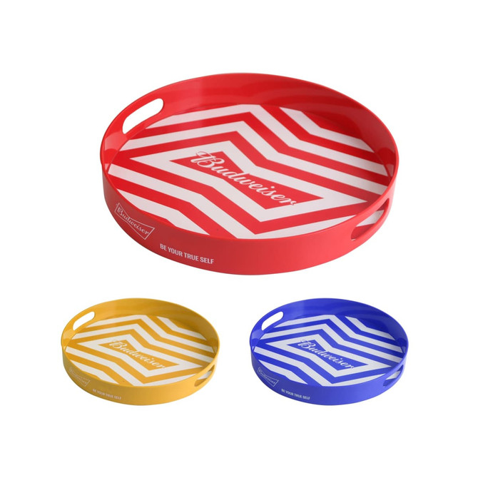 A set of three round serving trays in red, yellow, and blue with geometric patterns and handles. Each tray features a logo.