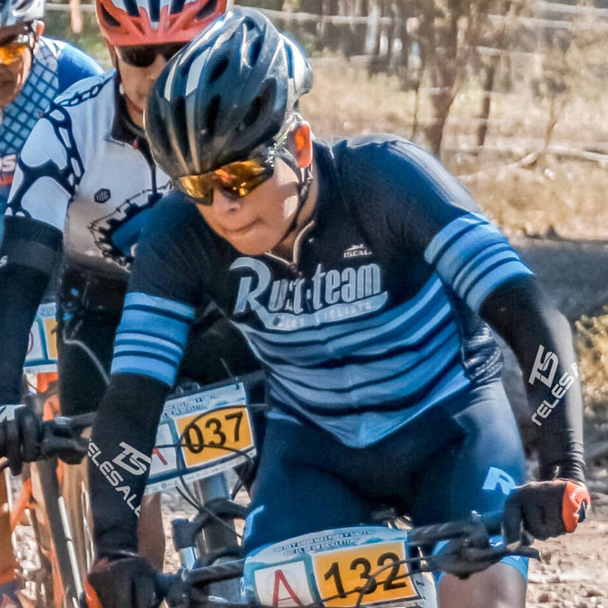 Three cyclists in helmets and sports attire, riding bikes on a dirt path. One is wearing a blue and black jersey.