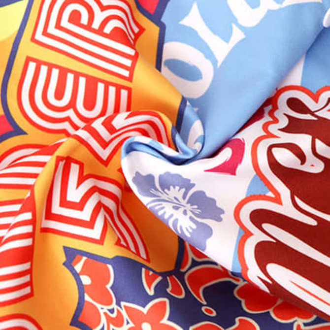 A vibrant, multicoloured fabric featuring various patterns, suitable for sublimation hooded towels. It has a branding logo.