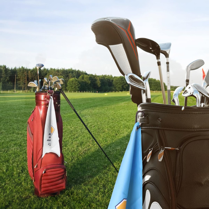 A red golf bag and a black golf bag sit on green grass, featuring clubs and a golf towel hanging from one bag.
