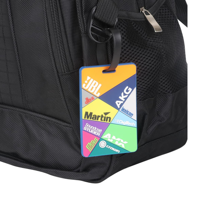 A custom-shaped PVC luggage tag in vibrant colours, attached to a black bag, featuring various logos.