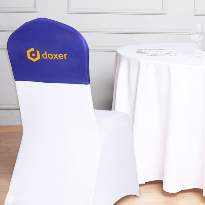 A half chair cover in blue and white featuring a logo, placed on a chair next to a table with a white tablecloth.