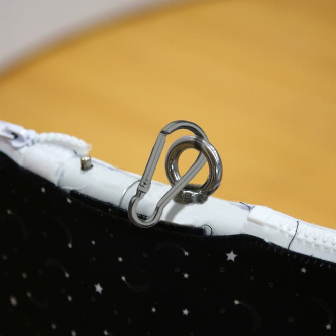 A round hanging banner with a black fabric featuring stars and moons, showcasing a silver carabiner clip.