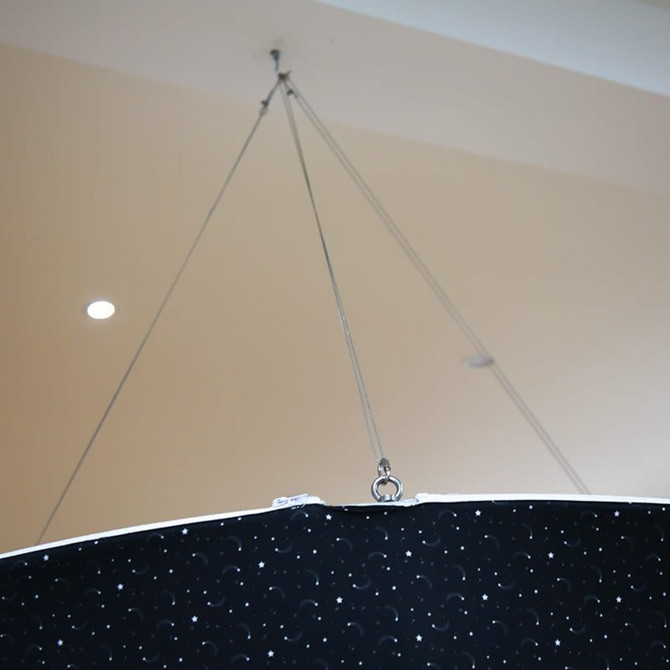 A round hanging banner in black with a patterned surface, suspended by metallic wires from the ceiling.