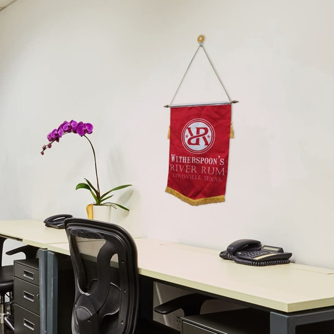 A red podium flag with gold fringe hanging on a wall above a desk, alongside an orchid plant and telephones.