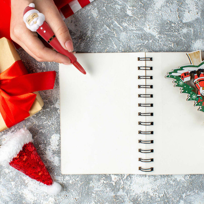 A red pen featuring a Santa stress reliever, surrounded by gifts, a blank notebook, and festive decorations.