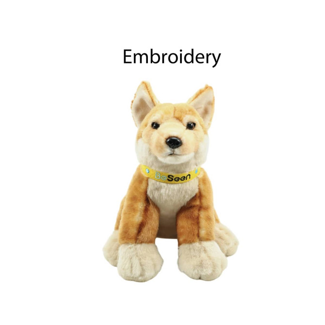 A plush Dingo toy in tan and cream, featuring embroidered details and a logo collar.