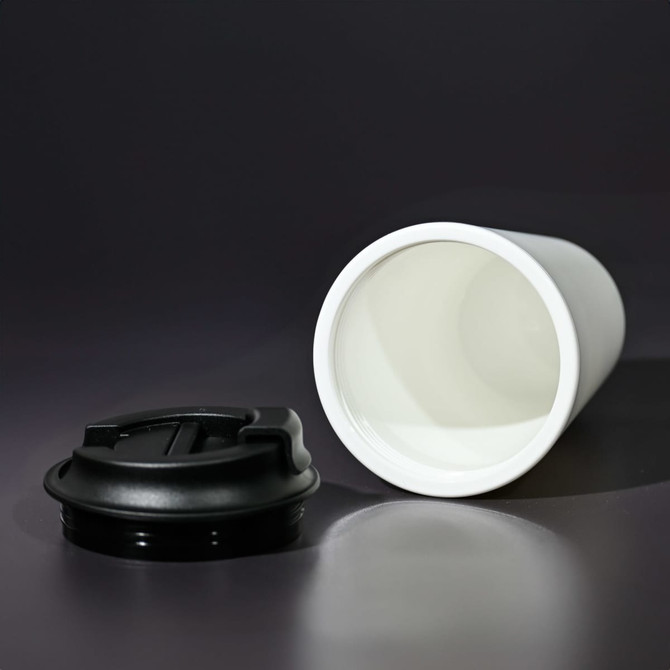 A white coffee mug made from recycled materials, featuring a black lid, displayed on a dark background.