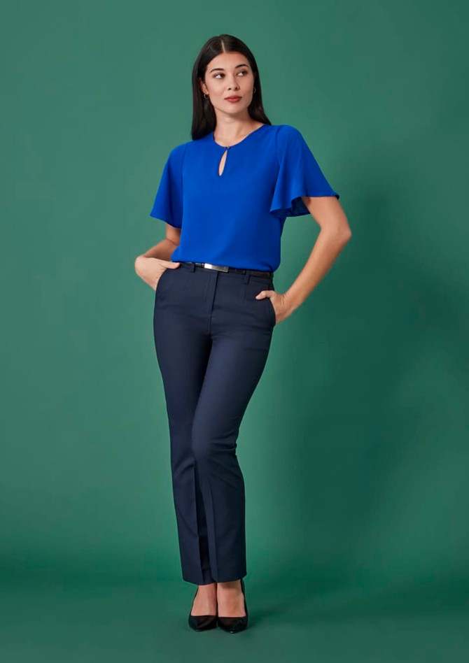 A model wearing navy tapered adjustable waist pants paired with a blue top against a green background.