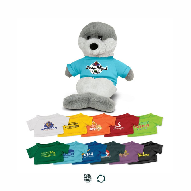 A grey and white seal plush toy wearing a blue T-shirt with a logo, positioned among colourful T-shirts in various shades.