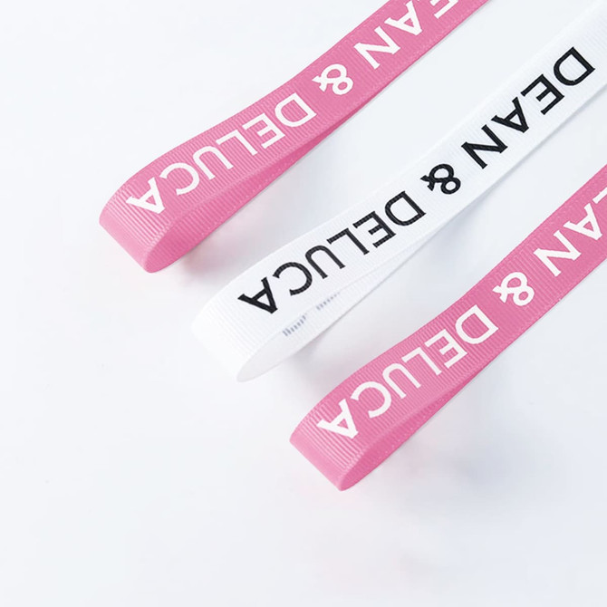 Ribbed fabric ribbon in pink and white, featuring a logo, suitable for various decorative uses.