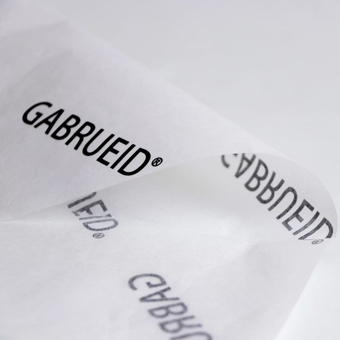 Kraft paper in white featuring a repeating black logo design, folded to display its texture and branding.