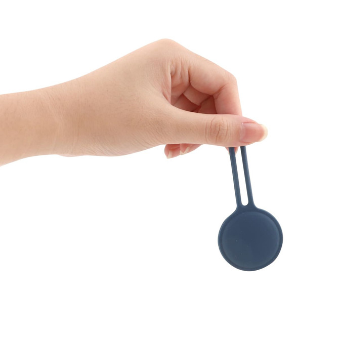 A hand holding a dark blue Air Tag protective case with a flat, rounded design and a attaching loop.