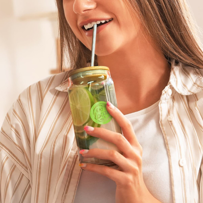 A glass tumbler with a gold lid and straw, filled with a drink and garnished with lime slices.