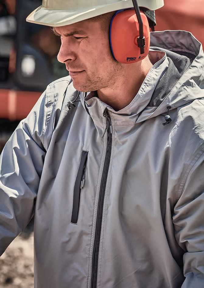 A man wearing a grey unisex packable rain jacket, with ear protection, outdoors in a work environment.
