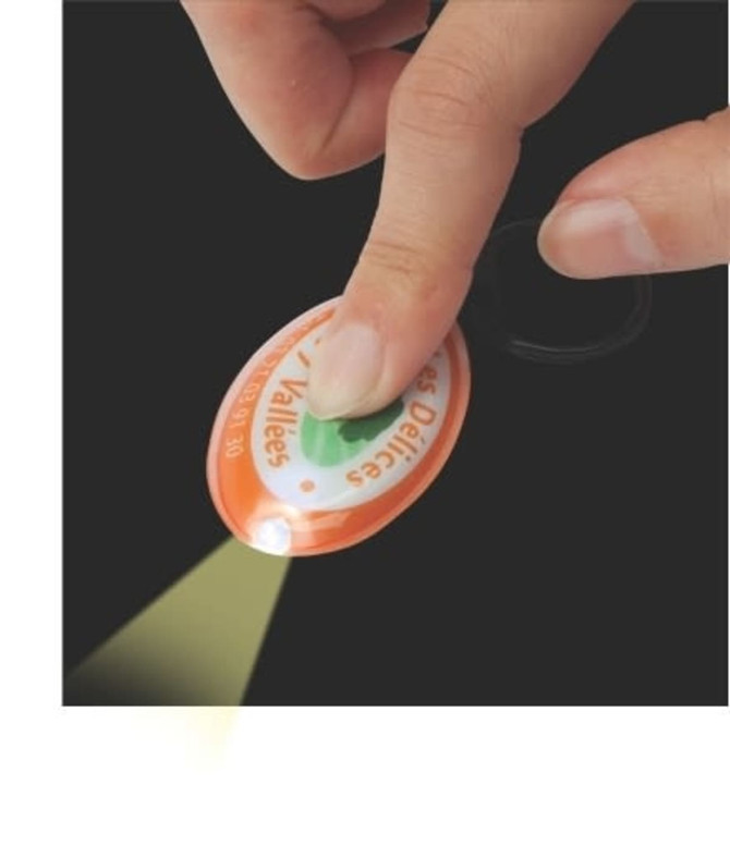 A hand pressing an orange press-light keyring, emitting light. The keyring features a logo on its surface.
