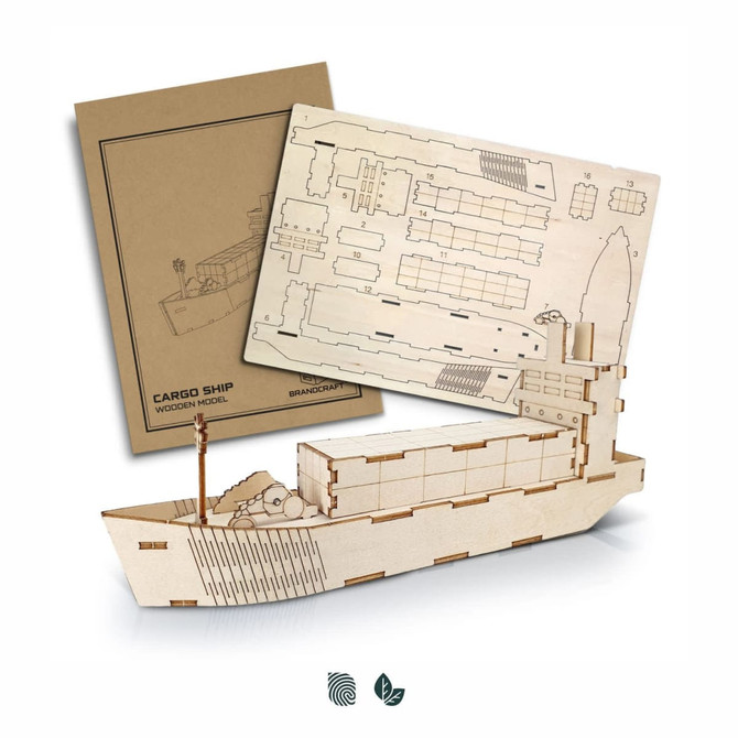 A wooden model of a cargo ship in a natural finish, alongside its assembly instructions, featuring a branding logo.
