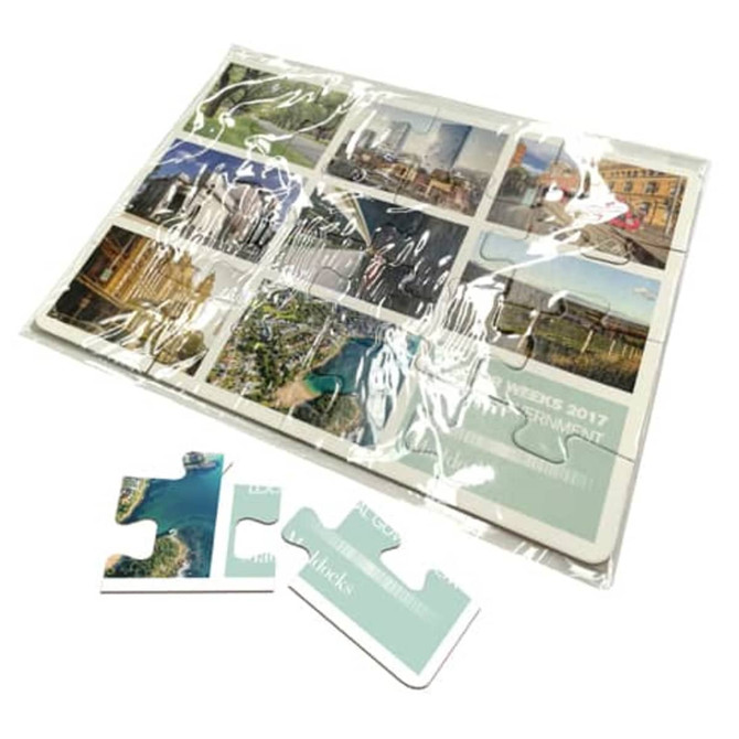 A5 cardboard jigsaw featuring colourful images of landscapes and cityscapes, packaged in clear plastic with puzzle pieces.