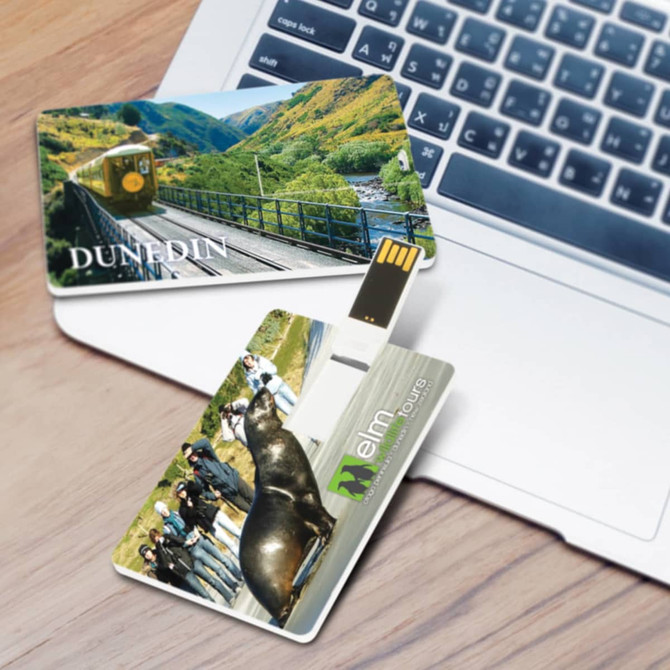A 4GB credit card-style flash drive with scenic images on both sides, placed near a laptop. Features colour graphics and branding.