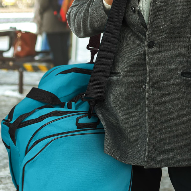 A turquoise duffle bag with black straps, held by a person in a grey coat, appears against a blurred background.