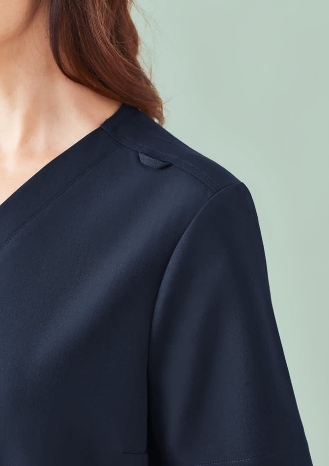 A close-up of a women's navy V-neck scrub top, featuring a slight shoulder detail and a branding logo.