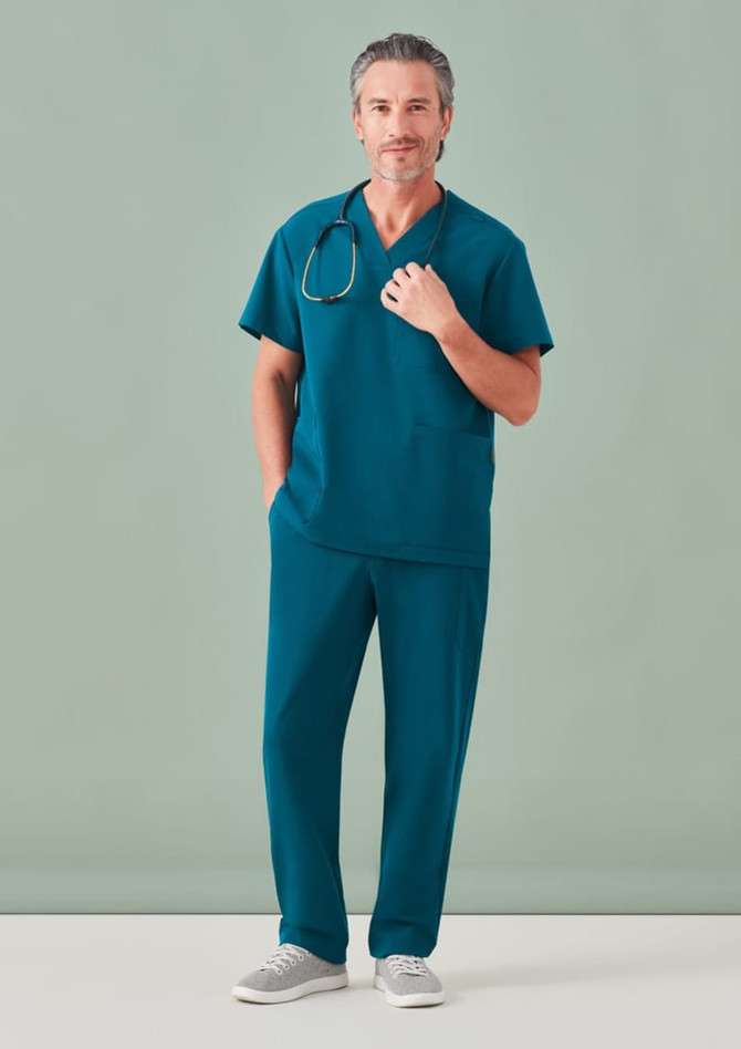 A man wearing teal unisex scrub pants and a matching scrub top, with a stethoscope around his neck.