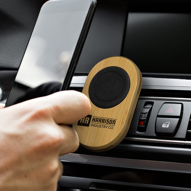 A bamboo car phone holder with a black circular grip, placed in a car dashboard vent, holding a smartphone.