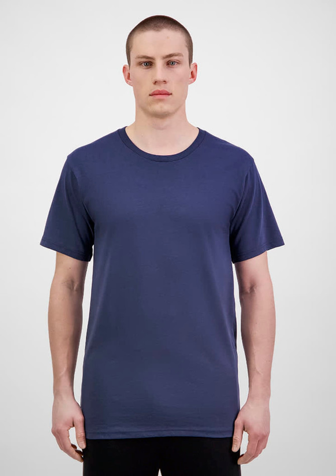 A man wearing a navy blue short sleeve tee, standing against a light grey backdrop. The tee has a logo.