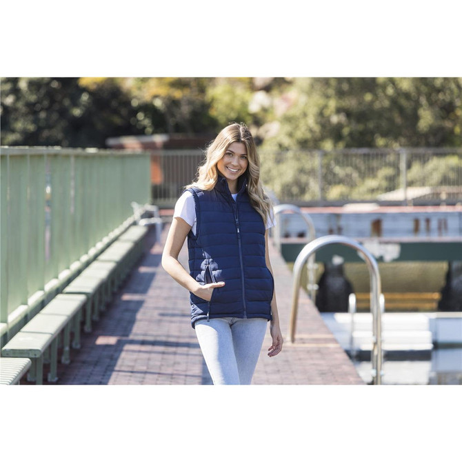 A unisex navy puffer vest worn by a model, featuring a front zip and pockets, set by a scenic outdoor backdrop.