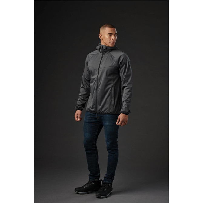 A man wearing a grey softshell jacket stands against a dark background, showcasing a sleek design and fitted style.
