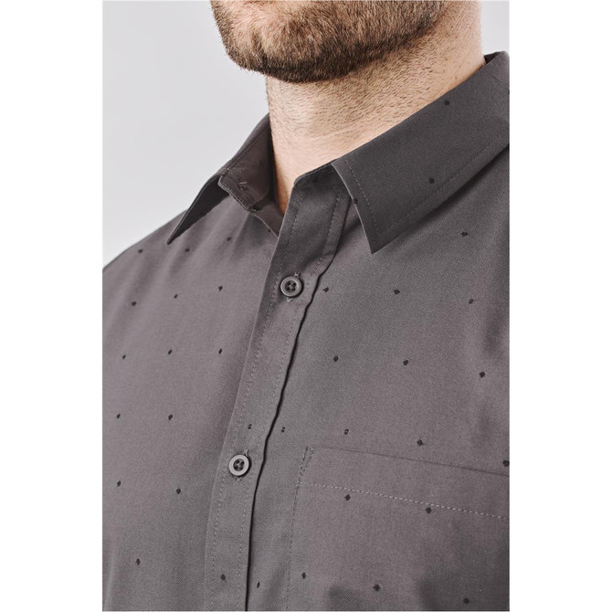 A close-up of a grey button-up shirt featuring a subtle dot pattern and a chest pocket. It has a logo on the label.
