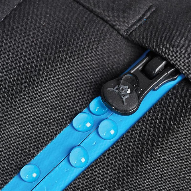 A close-up of a black softshell jacket zipper featuring a blue waterproof lining and droplets of water.