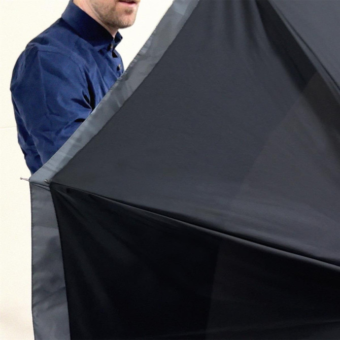 A black umbrella being held by a person wearing a blue shirt. The umbrella features a sleek design and has branding.