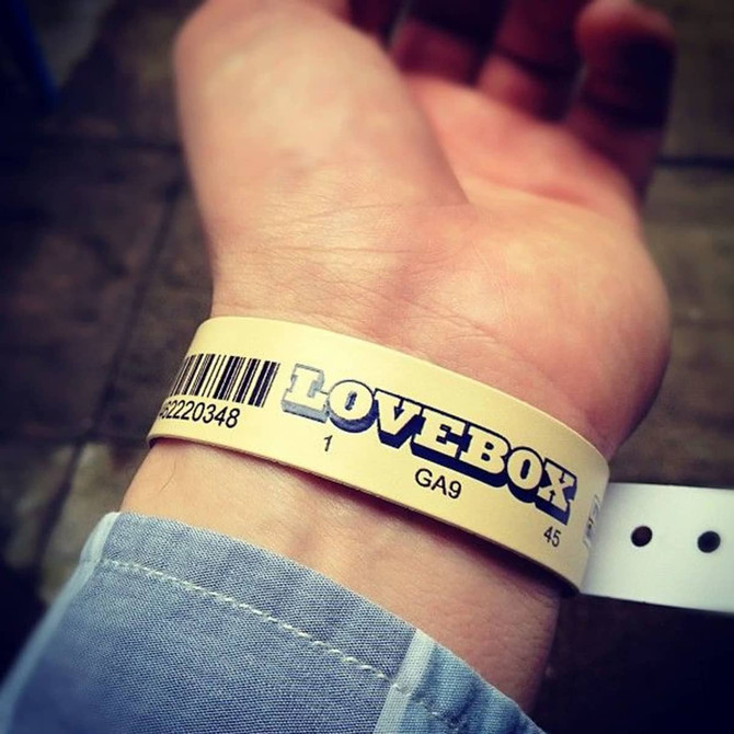 A vinyl wristband in cream with a barcode and branding, worn on a person's wrist.
