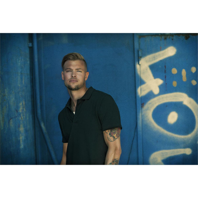 A men's cotton polo in dark green with a subtle logo, displayed against a blue background.