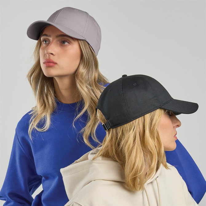 Two women wearing caps, one grey and one black, both styled with casual clothing. The caps feature logos.