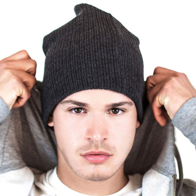 A grey ribbed beanie worn by a model with a neutral expression, holding up the hood of a jacket.