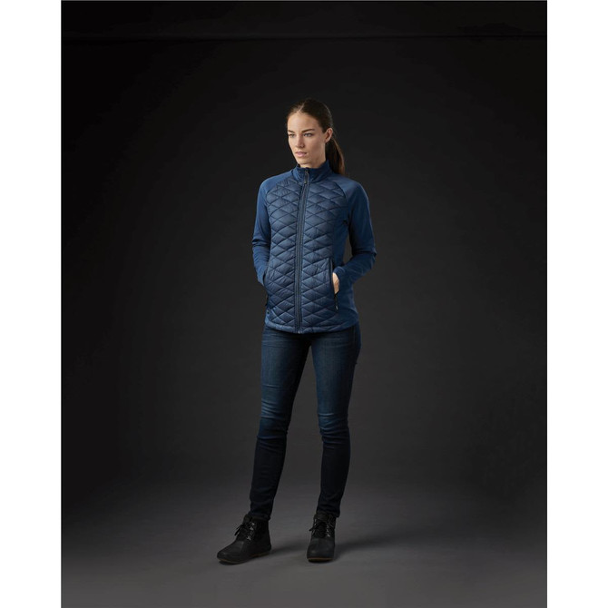 A women's boulder thermal shell jacket in dark blue with a quilted design and pockets, displayed against a dark background.