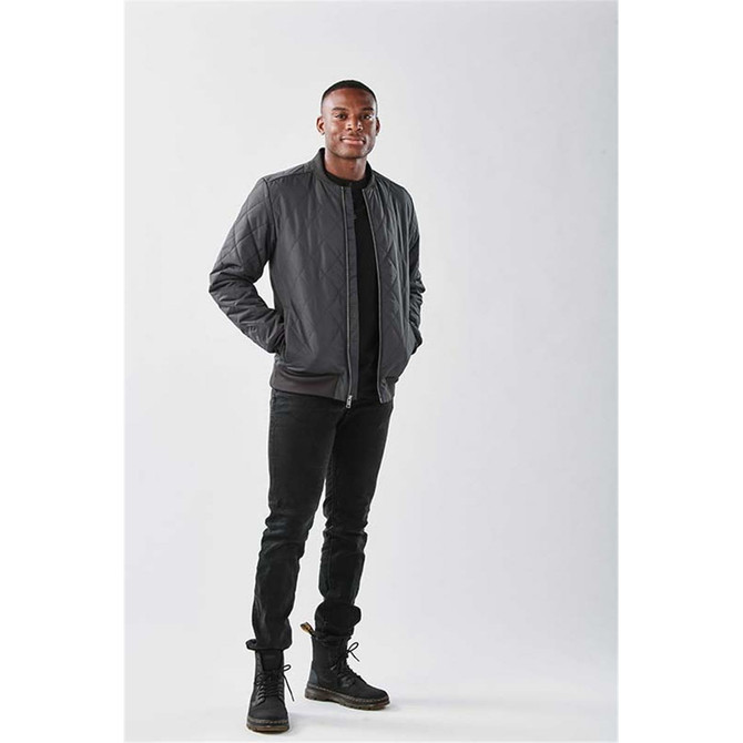 A men's thermal jacket in dark grey, featuring a quilted design and a branded logo, paired with black jeans and boots.