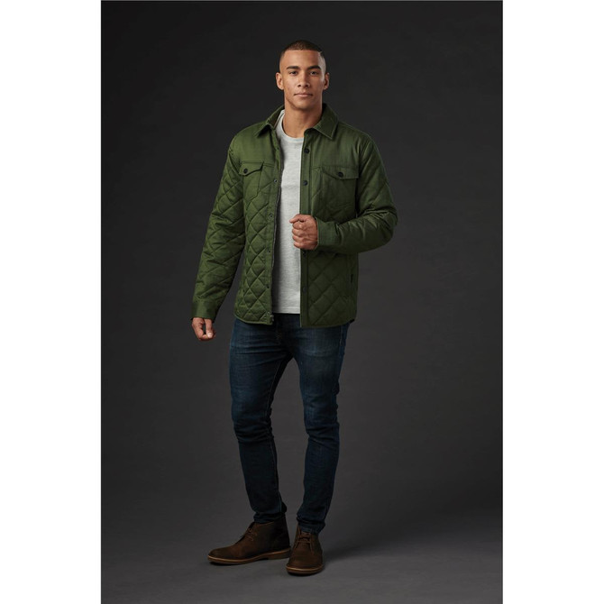 A man models a men's quilted jacket in olive green, paired with a light top, jeans, and boots. The jacket has a logo.