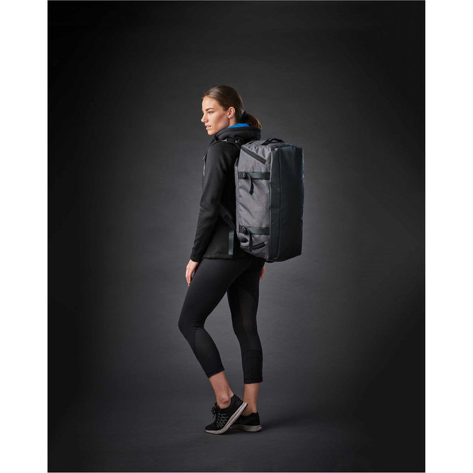 A woman in athletic wear stands sideways, carrying a grey Equinox 30 duffel bag with a logo.