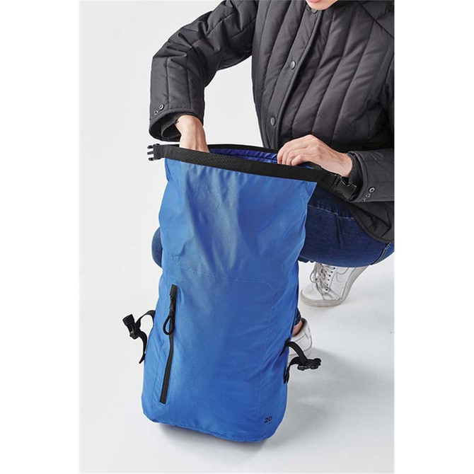 A blue roll-top backpack displayed with a person opening the top, featuring adjustable straps and a zippered pocket.