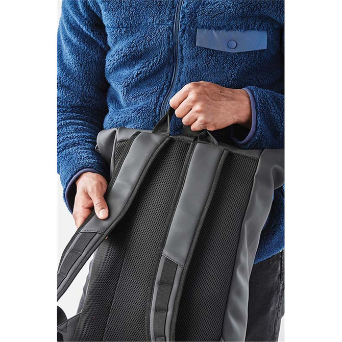 A person holds a black Sargasso Backpack with padded straps, wearing a blue fleece jacket.