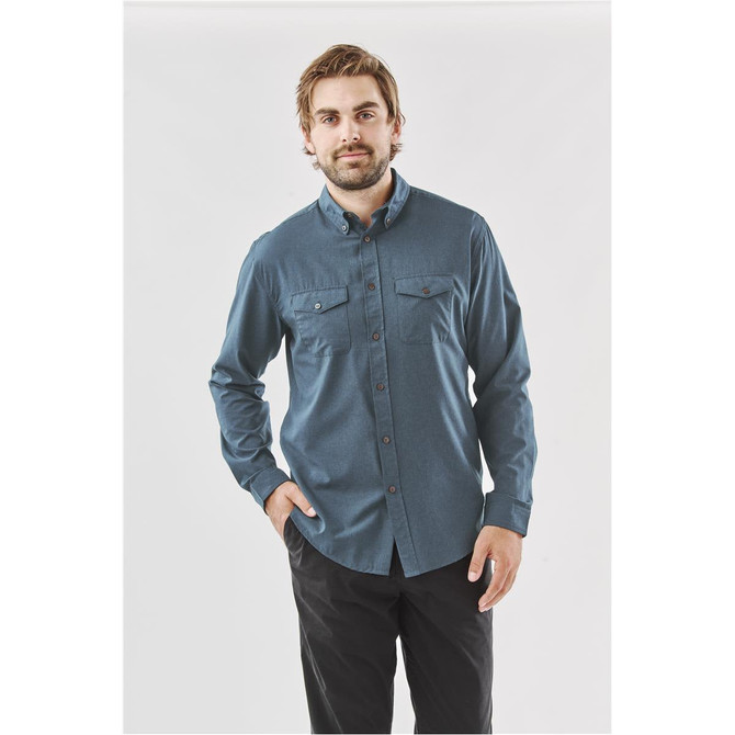 A model wearing a men's long-sleeve shirt in blue, featuring two chest pockets and a button-down collar.