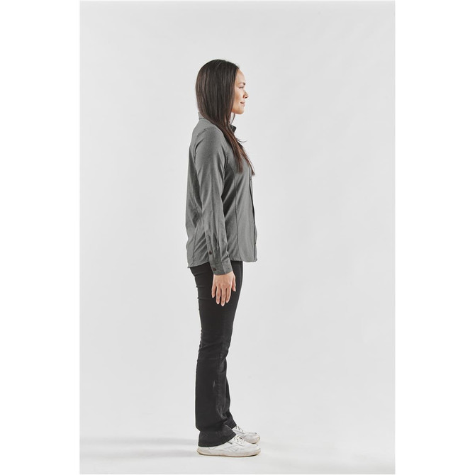 A side view of a woman wearing a grey button-up shirt and black pants, standing against a white background.