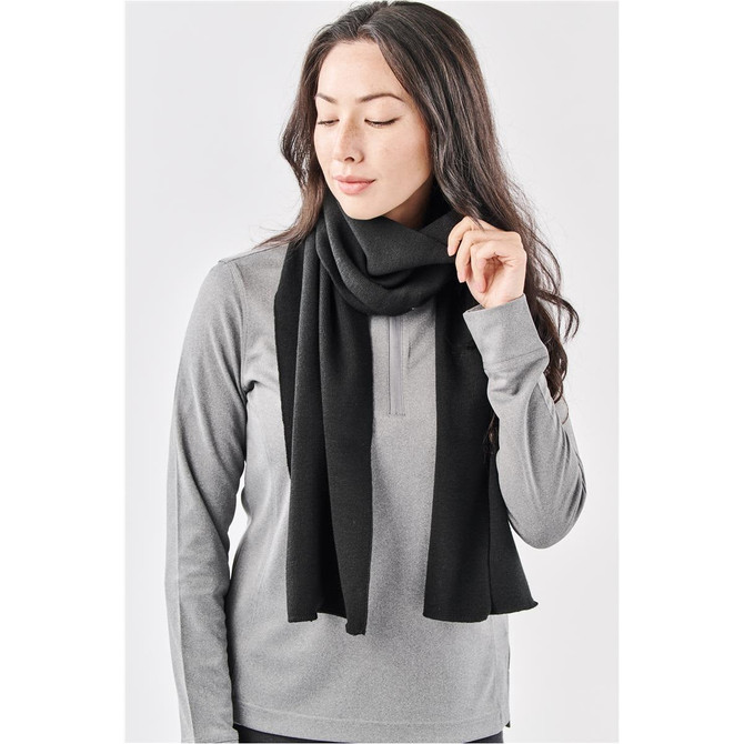 A woman models a black knit scarf, styled casually with a grey top. The scarf has a soft texture and falls loosely.